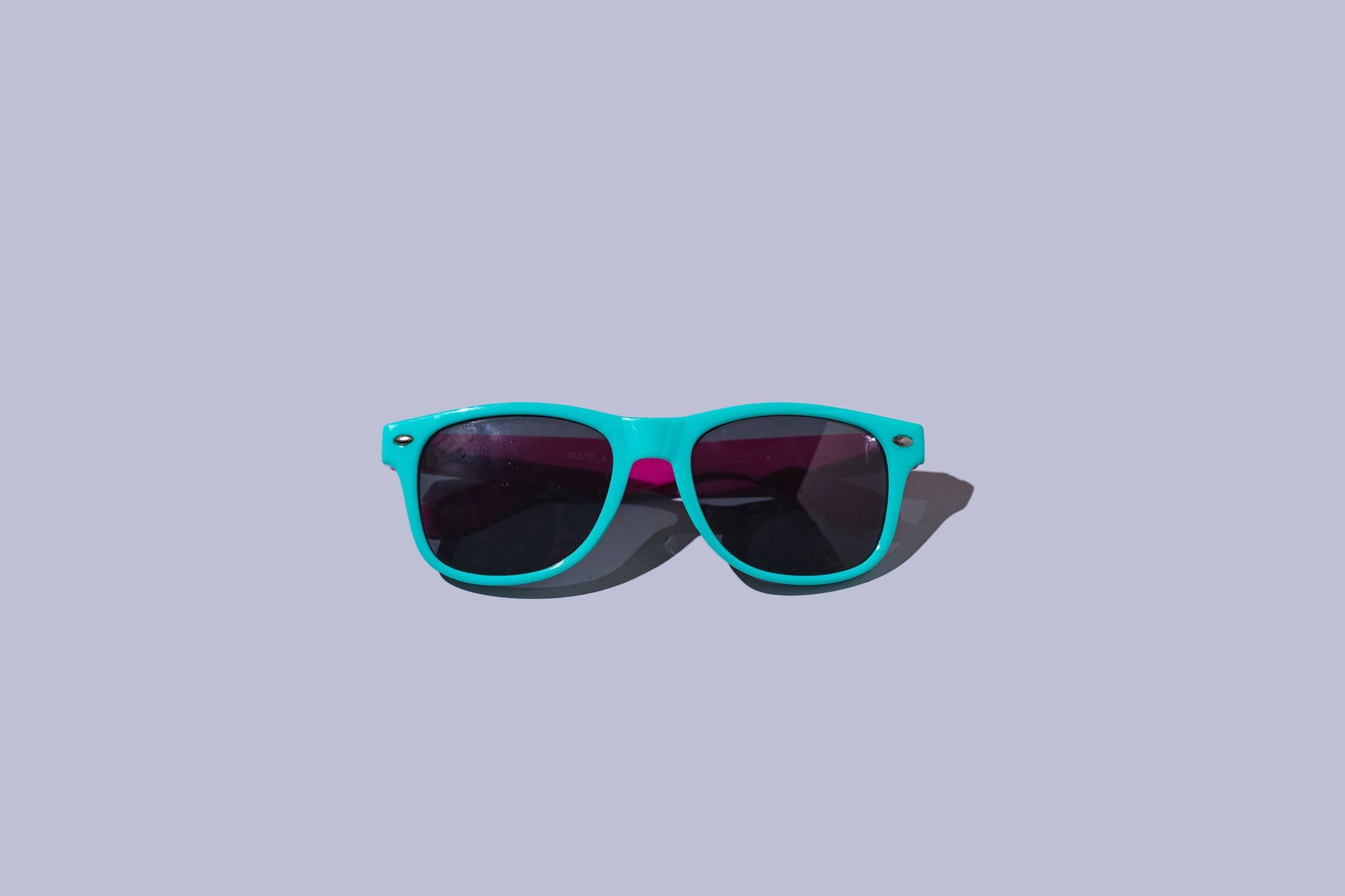 Teal sunglasses with pink accents on a light purple background.