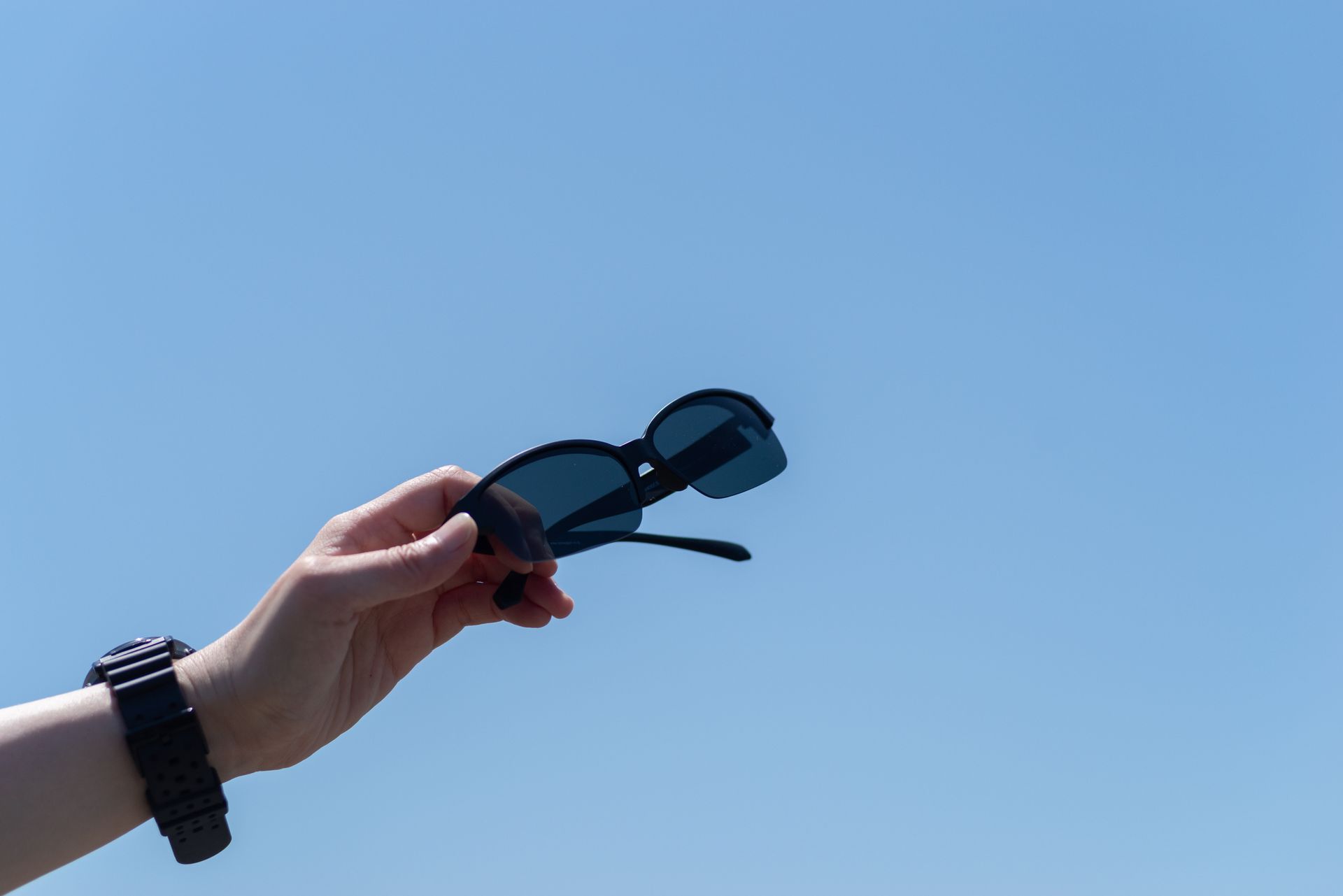 Hand holding sunglasses against a blue sky.