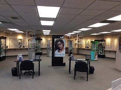 Interior of an optical shop with eyeglasses displays, desks, and a GUESS advertisement.