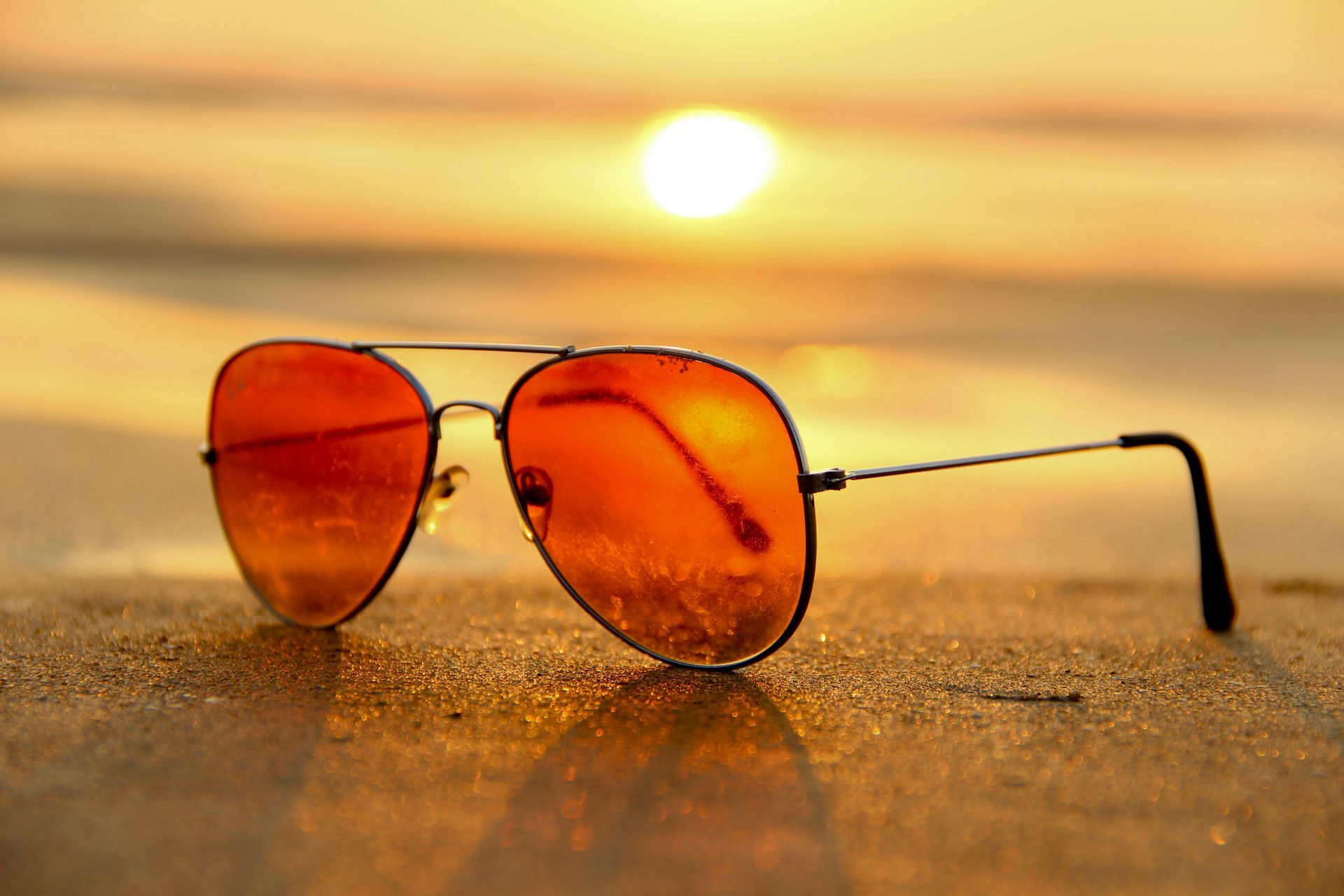A pair of sunglasses is sitting on the beach at sunset.
