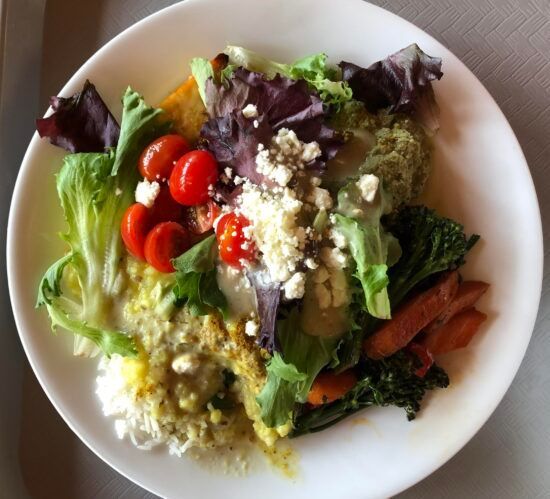 White plate of mixed salad with leafy greens, cherry tomatoes, crumbled cheese, and dressing