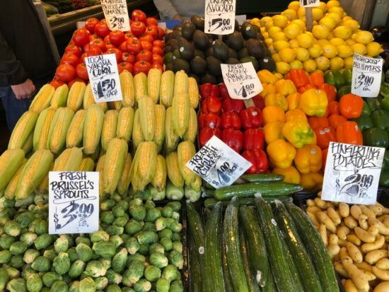 Colorful display of assorted fruits and vegetables with handwritten price signs at a market.
