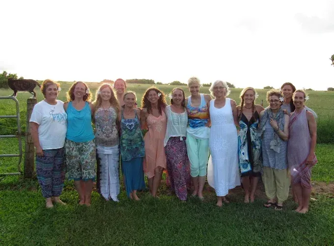 Group of people standing together outdoors on grass at sunset, smiling at the camera.
