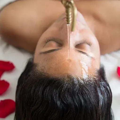 Person receiving a forehead oil pour during a spa treatment, lying face-up on a massage table