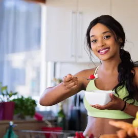 Woman in a kitchen smiling while holding a bowl and spoon with strawberries.