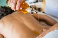 Massage therapist using a wooden tool on a person’s bare back and shoulder area