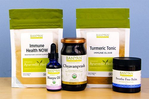 Ayurvedic health product display with two white-and-green bags, tincture dropper, jar, and small black-lidded container