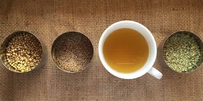 Assorted loose teas in small bowls around a cup of brewed tea on a wooden surface