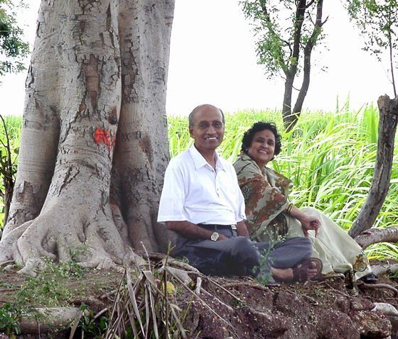 Couple sitting under a large tree in a grassy field, smiling beside exposed roots.