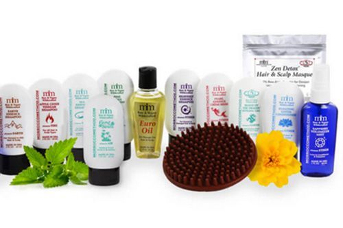 Assorted hair care products and tools arranged in a row, including bottles, tubes, a scalp massager, and flowers