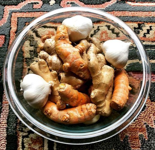 Bowl of fresh turmeric roots and garlic cloves on a patterned cloth