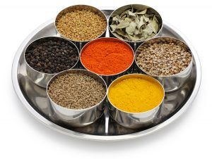 Tray of stainless steel spice bowls with assorted colorful spices and herbs.