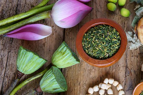 Assorted herbal ingredients and purple flowers arranged on a rustic wooden table, with a bowl of dried herbs
