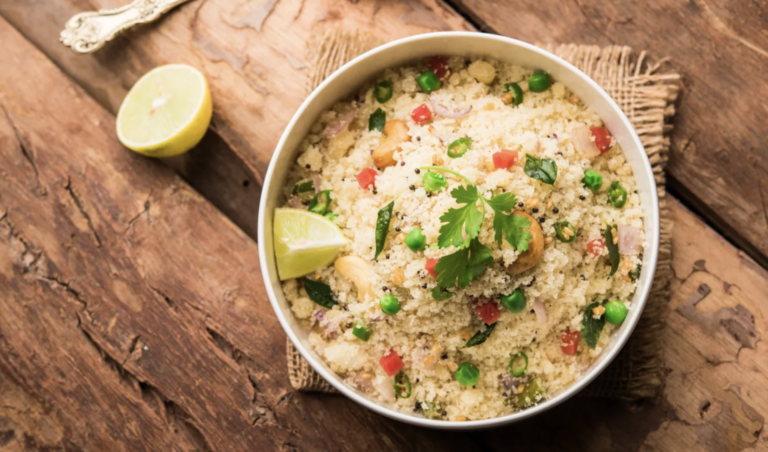 Bowl of couscous or rice salad topped with herbs and red peppers, with lime wedges on a wooden table