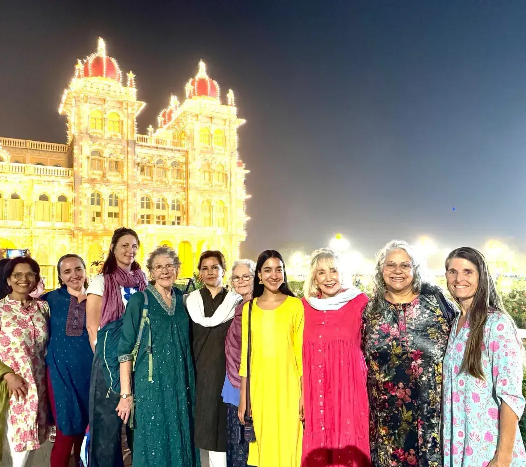 Group posing in front of a brightly lit ornate building at night, with colorful outfits and smiling faces