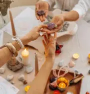 Hands exchanging crystals and incense around a lit, candlelit altar with ritual objects