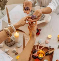 Hands exchanging crystals and incense around a lit, candlelit altar with ritual objects