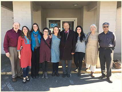 Nine people stand smiling outside a building entrance in daylight.