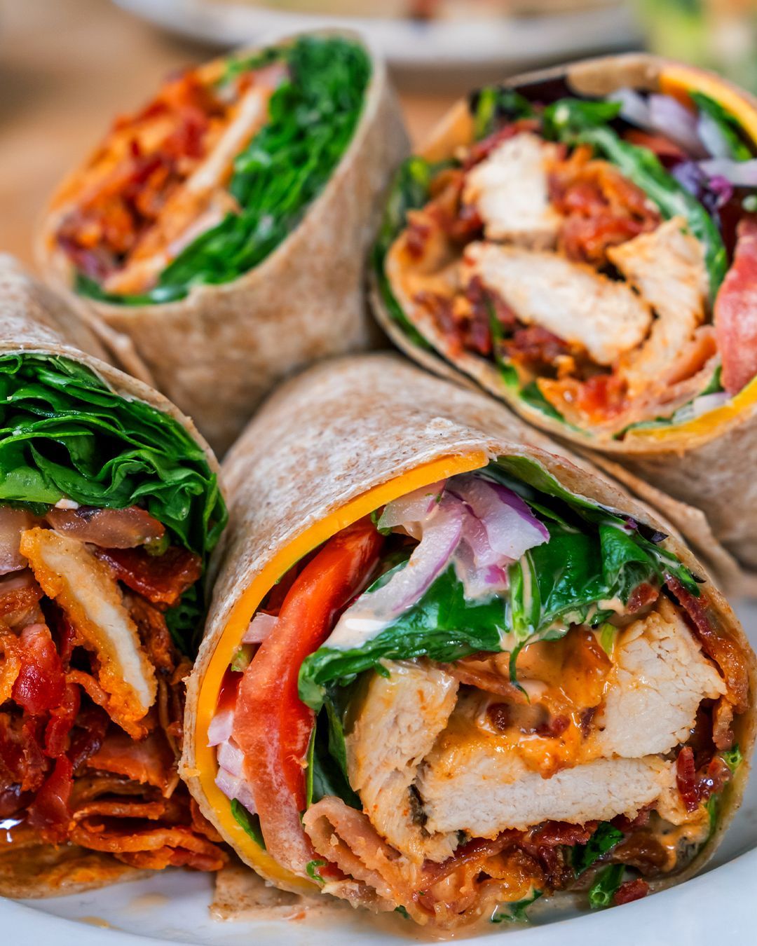 A close up of a plate of wraps with chicken and vegetables on a table.