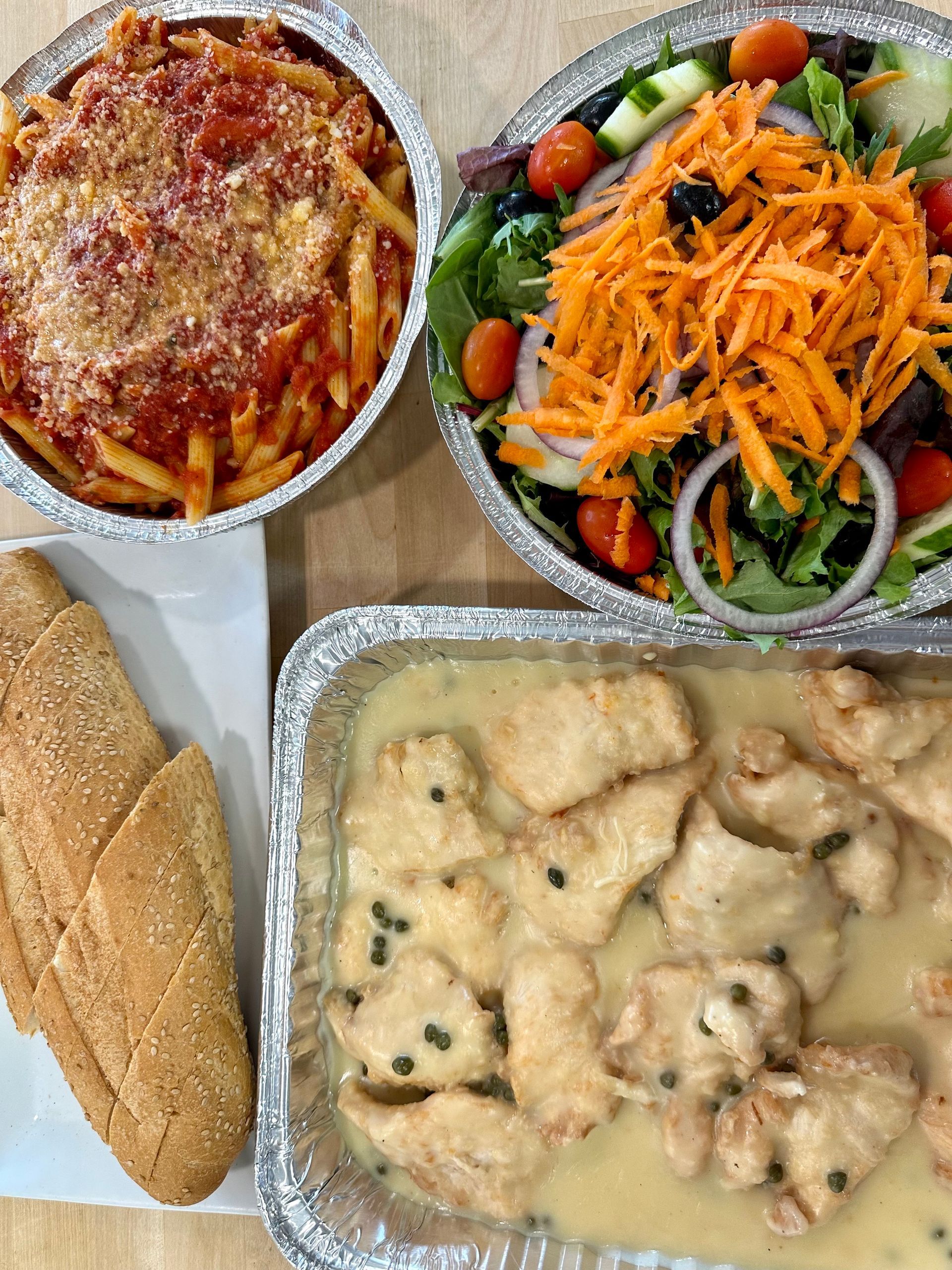 Pasta, salad, chicken in sauce, and bread in aluminum containers, ready for a meal.
