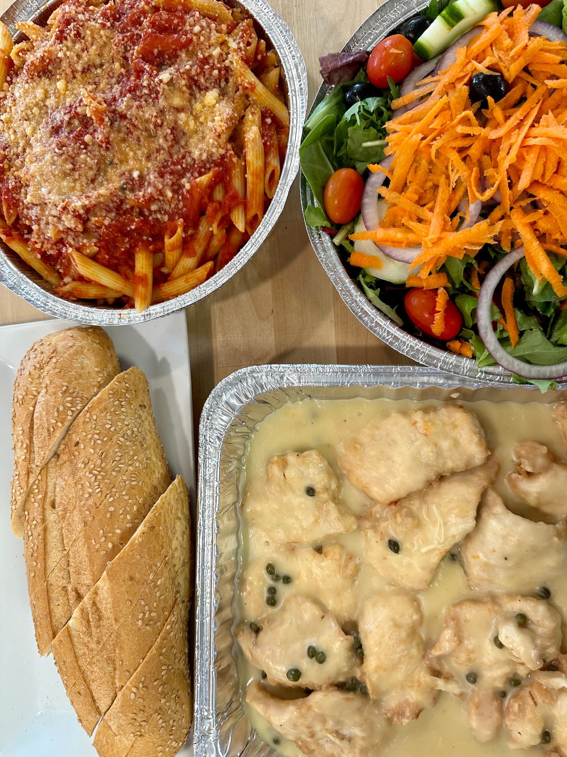 Italian dishes: pasta, salad, chicken with sauce, and bread in foil containers.