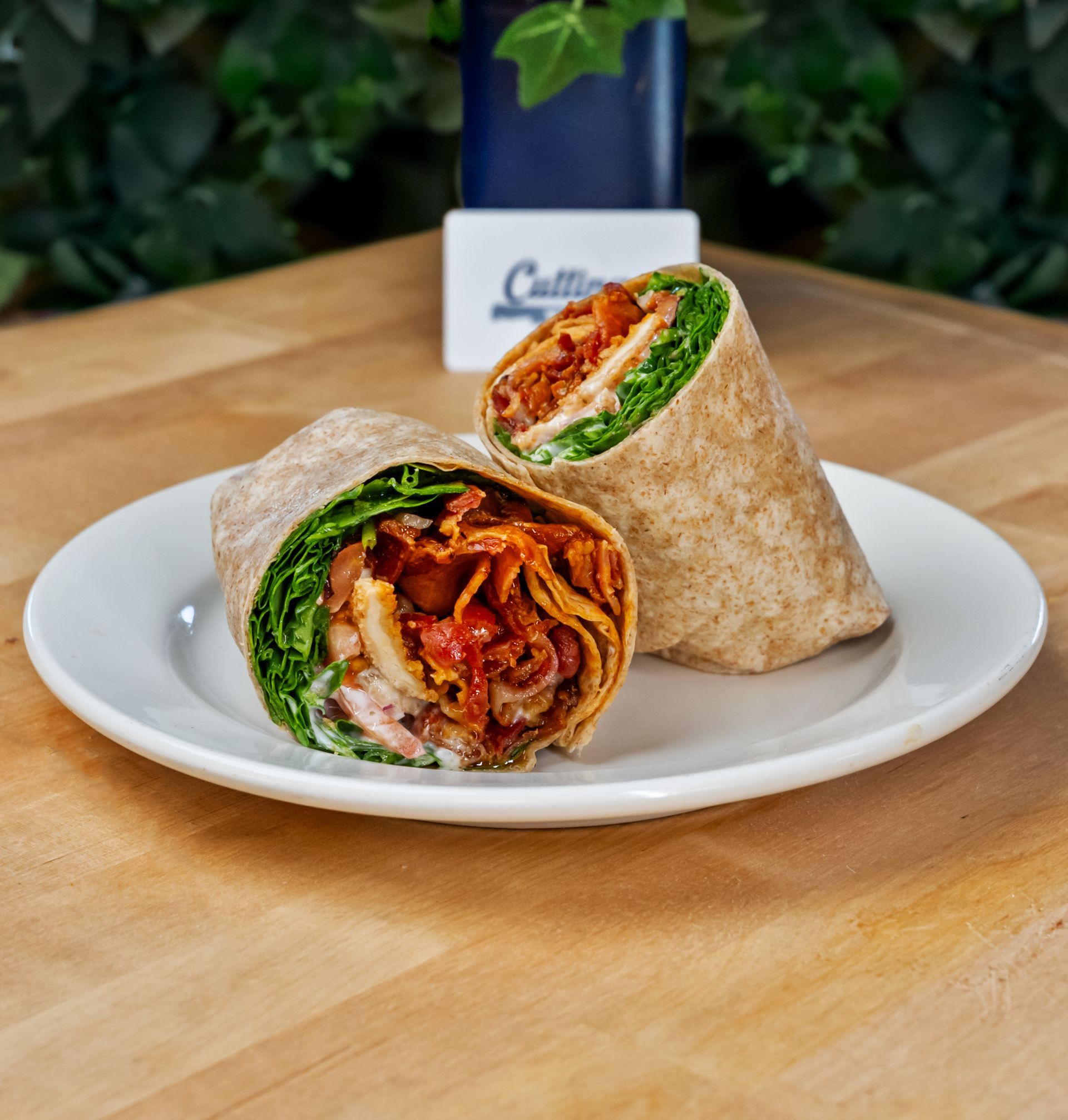 Two wraps are on a white plate on a wooden table.