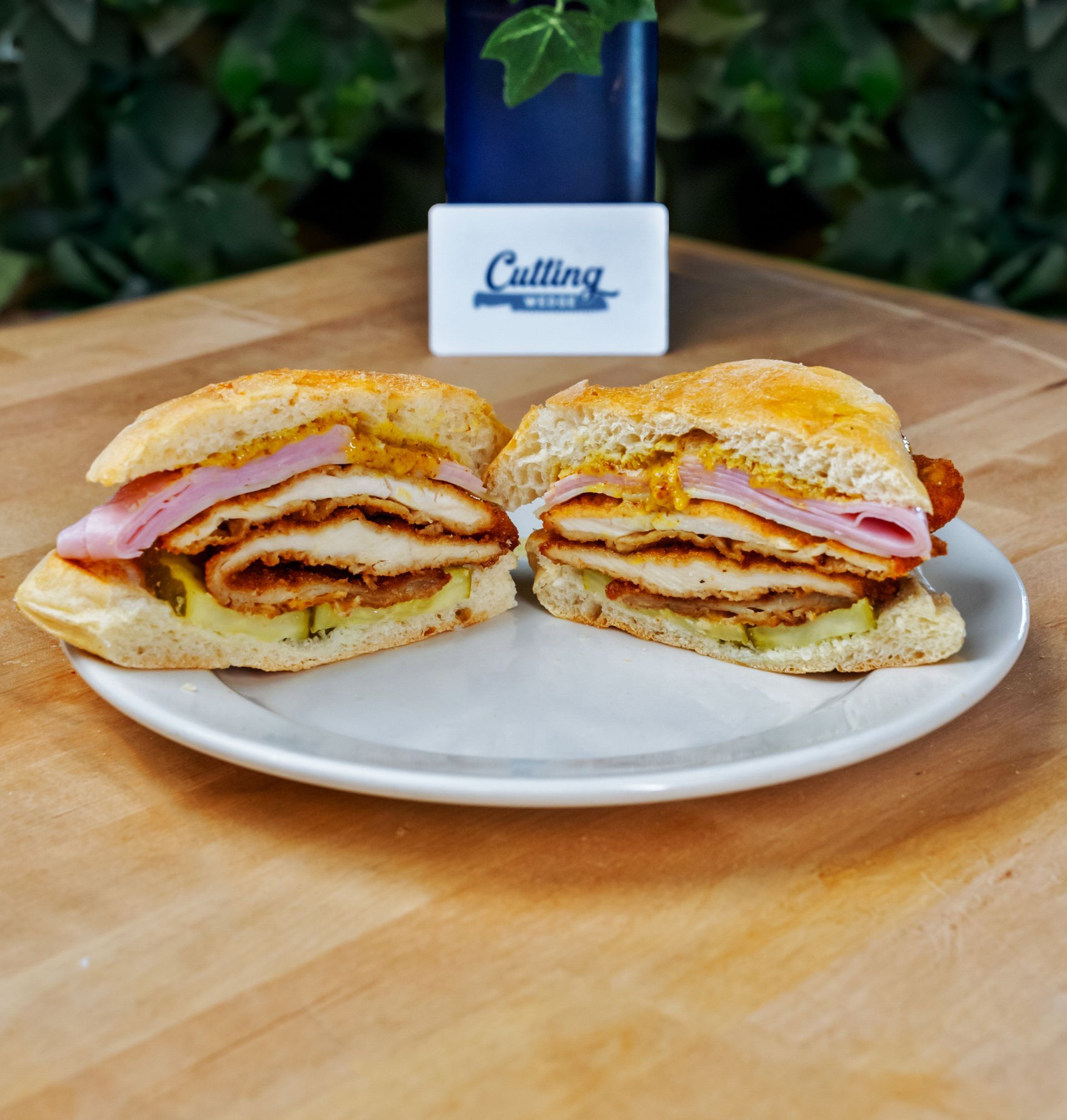 A sandwich is cut in half on a white plate on a wooden table.