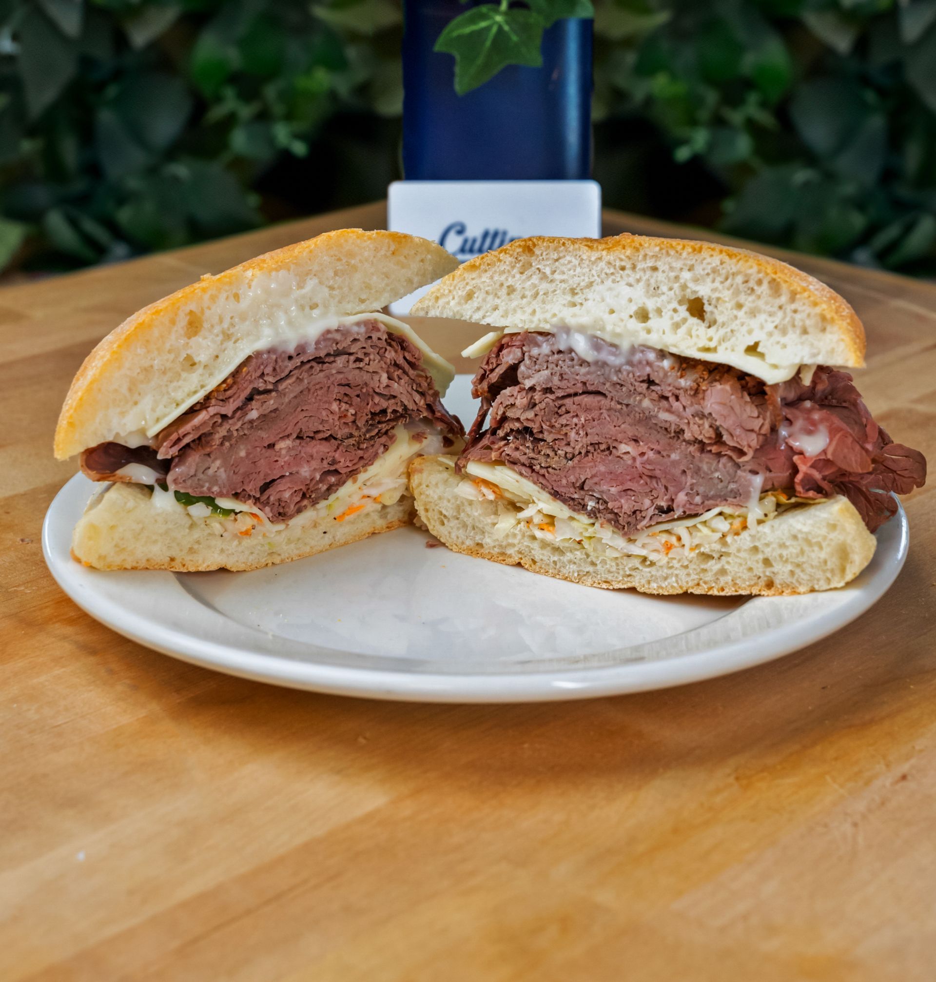 A roast beef sandwich is cut in half on a white plate on a wooden table.
