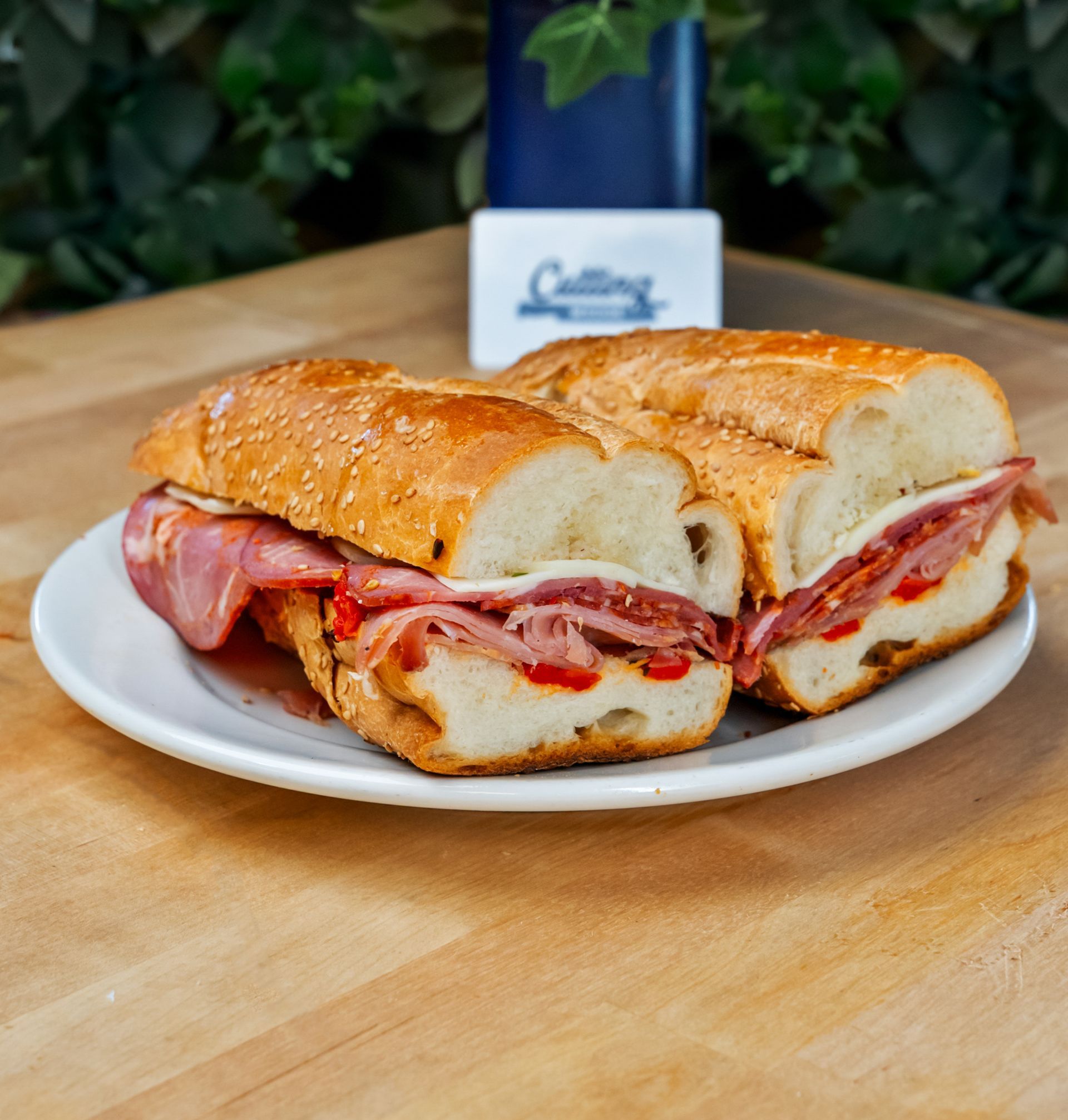 Two sub sandwiches are on a white plate on a wooden table.