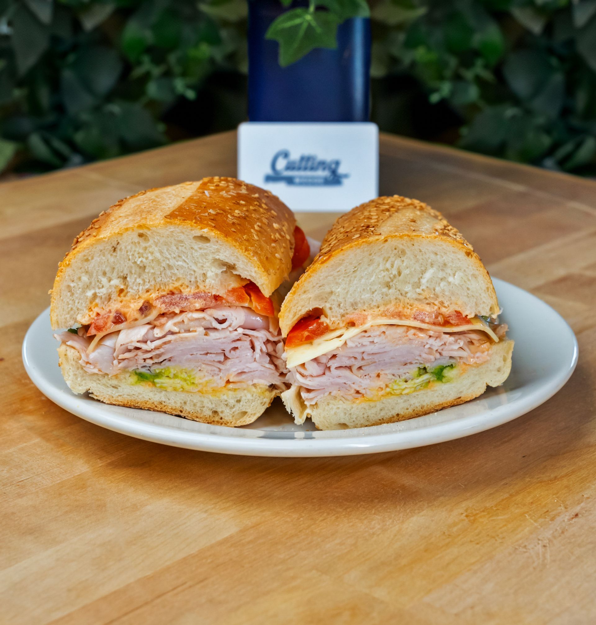 A sandwich is cut in half on a white plate on a wooden table.