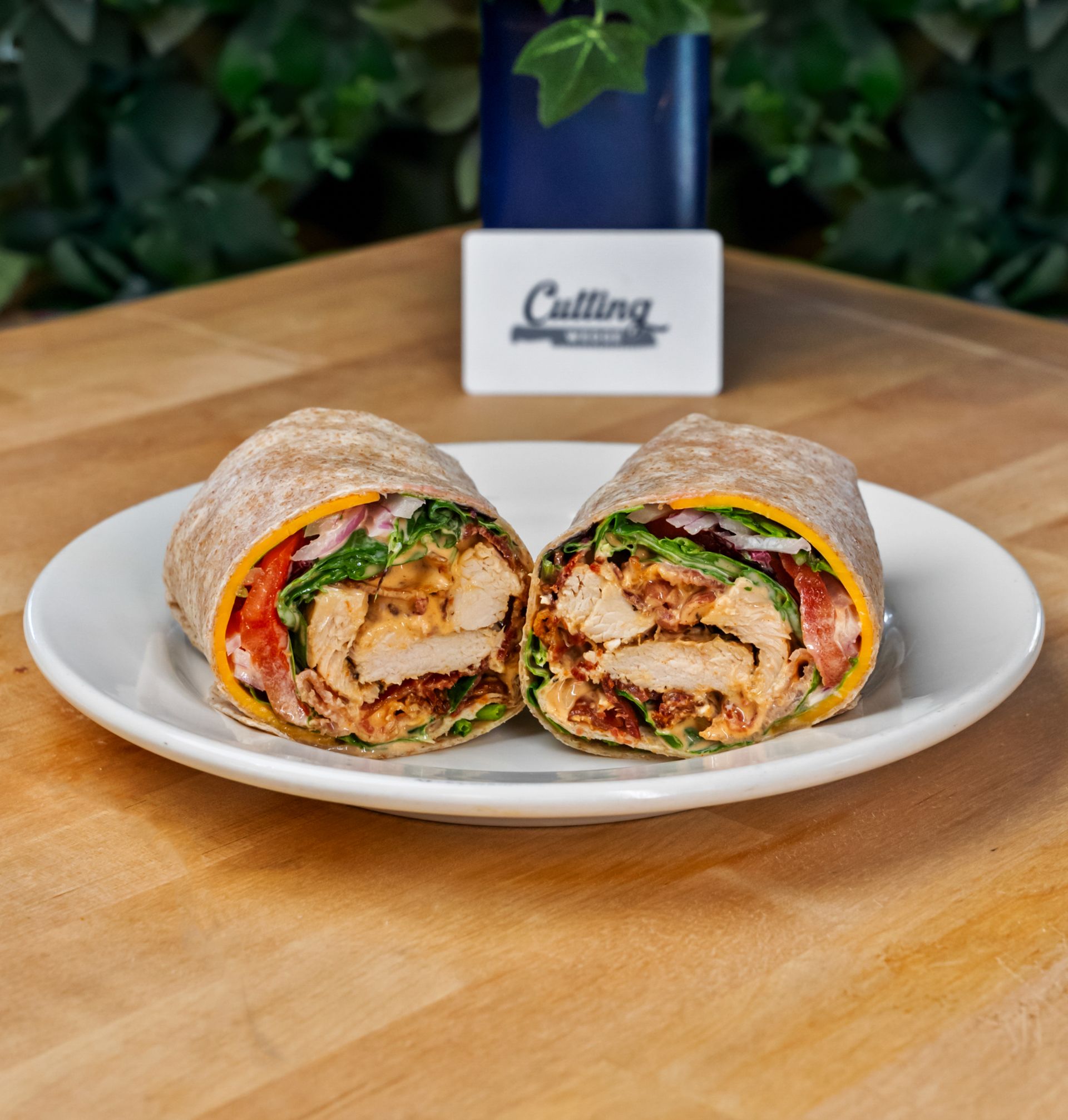 A chicken wrap is cut in half on a white plate on a wooden table.