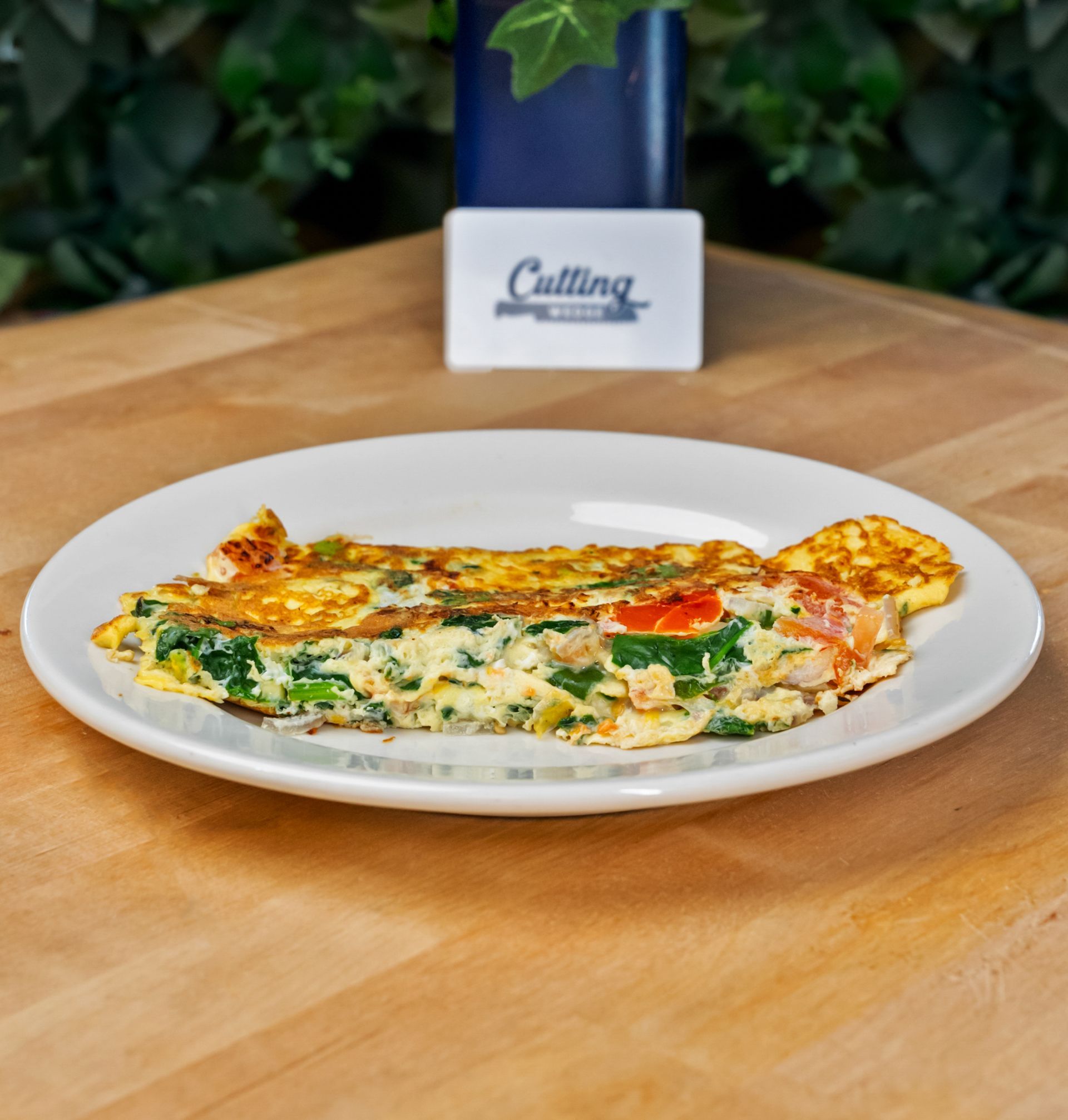 A white plate topped with an omelet is on a wooden table.