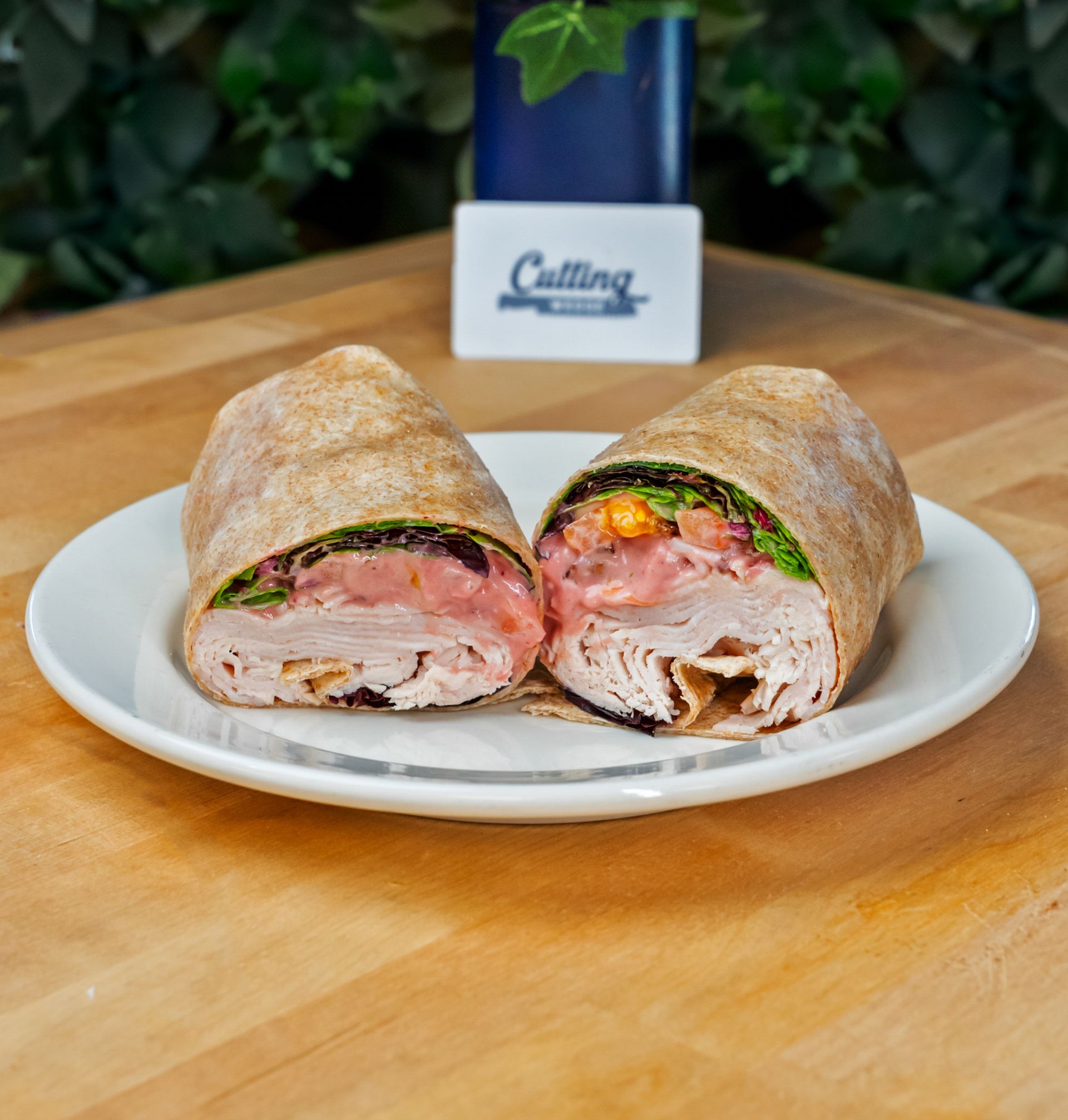 A turkey wrap is cut in half on a white plate on a wooden table.