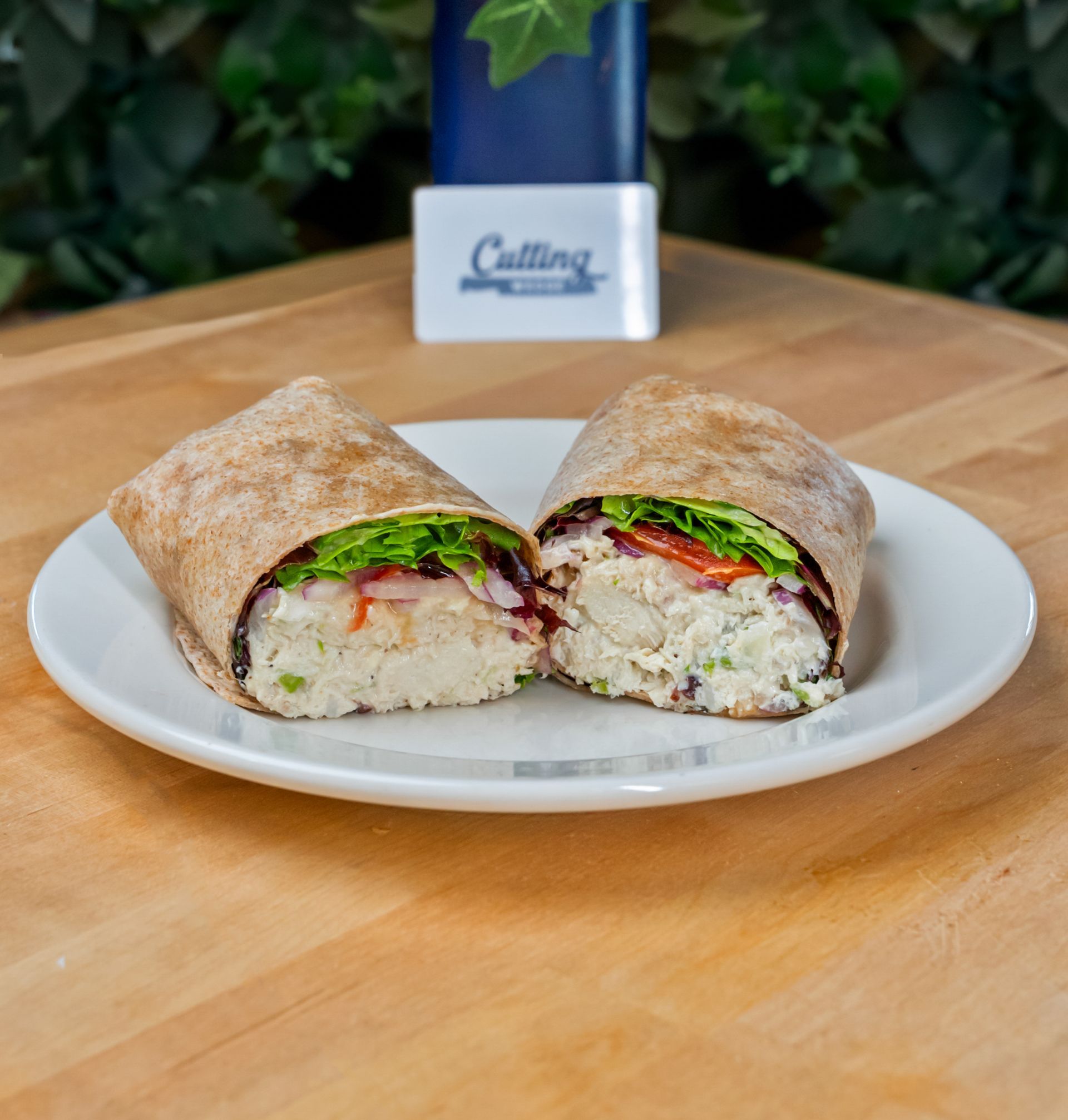 A wrap sandwich is cut in half on a white plate on a wooden table.