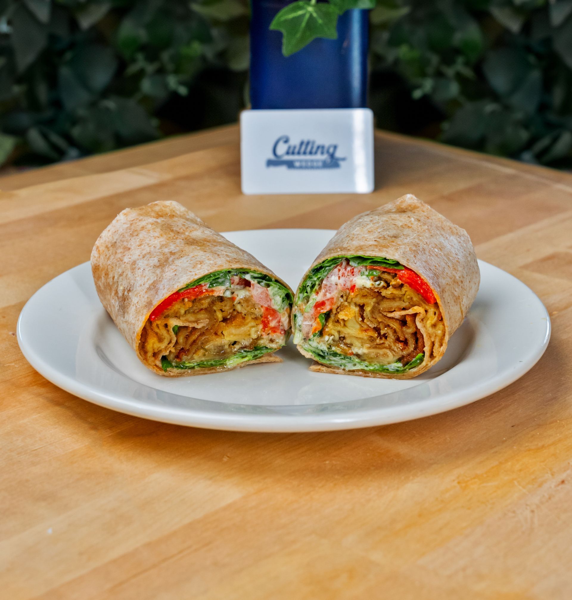 Two wraps are cut in half on a white plate on a wooden table.