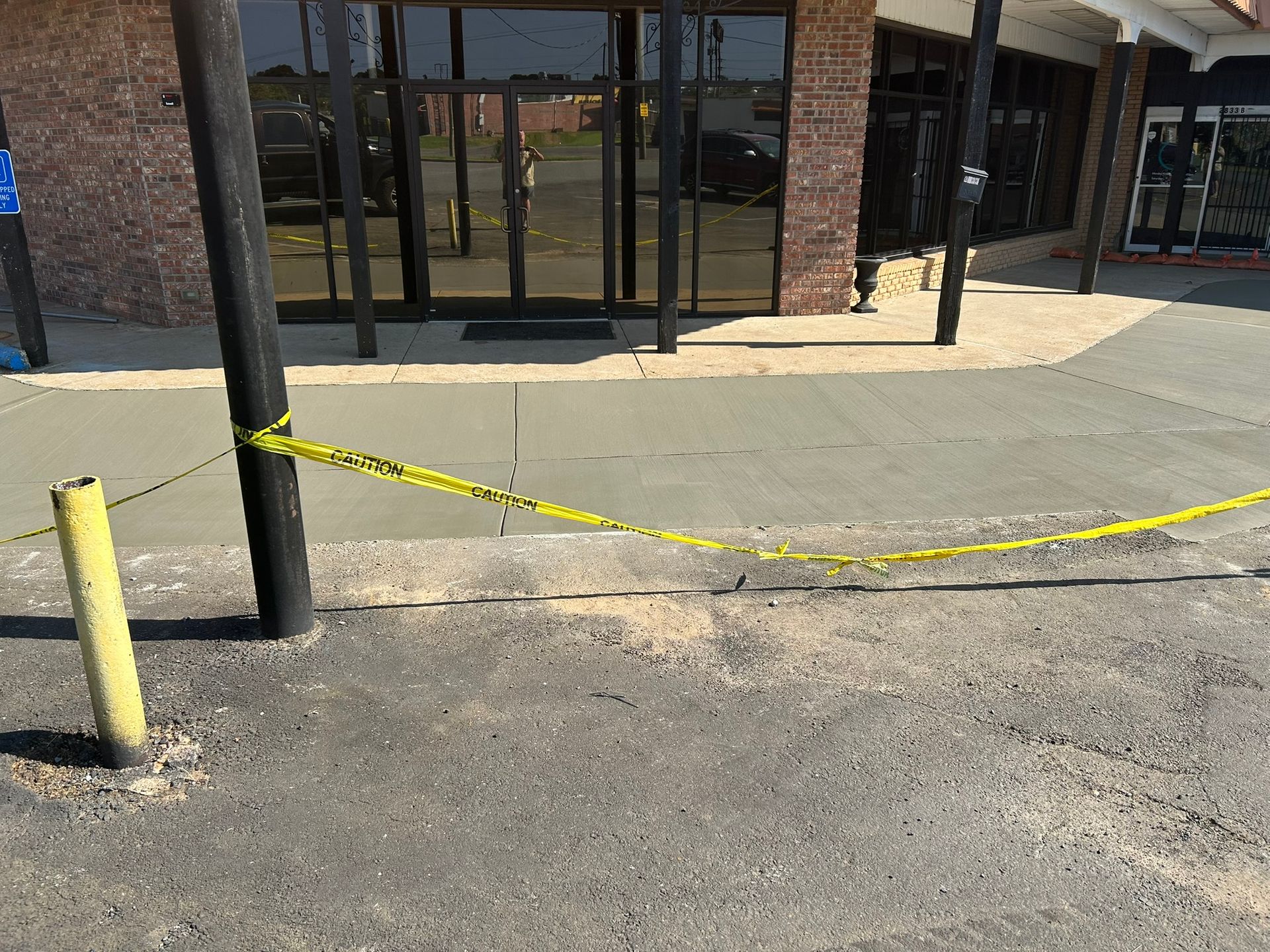A building entrance with wet concrete sidewalk, blocked by caution tape.