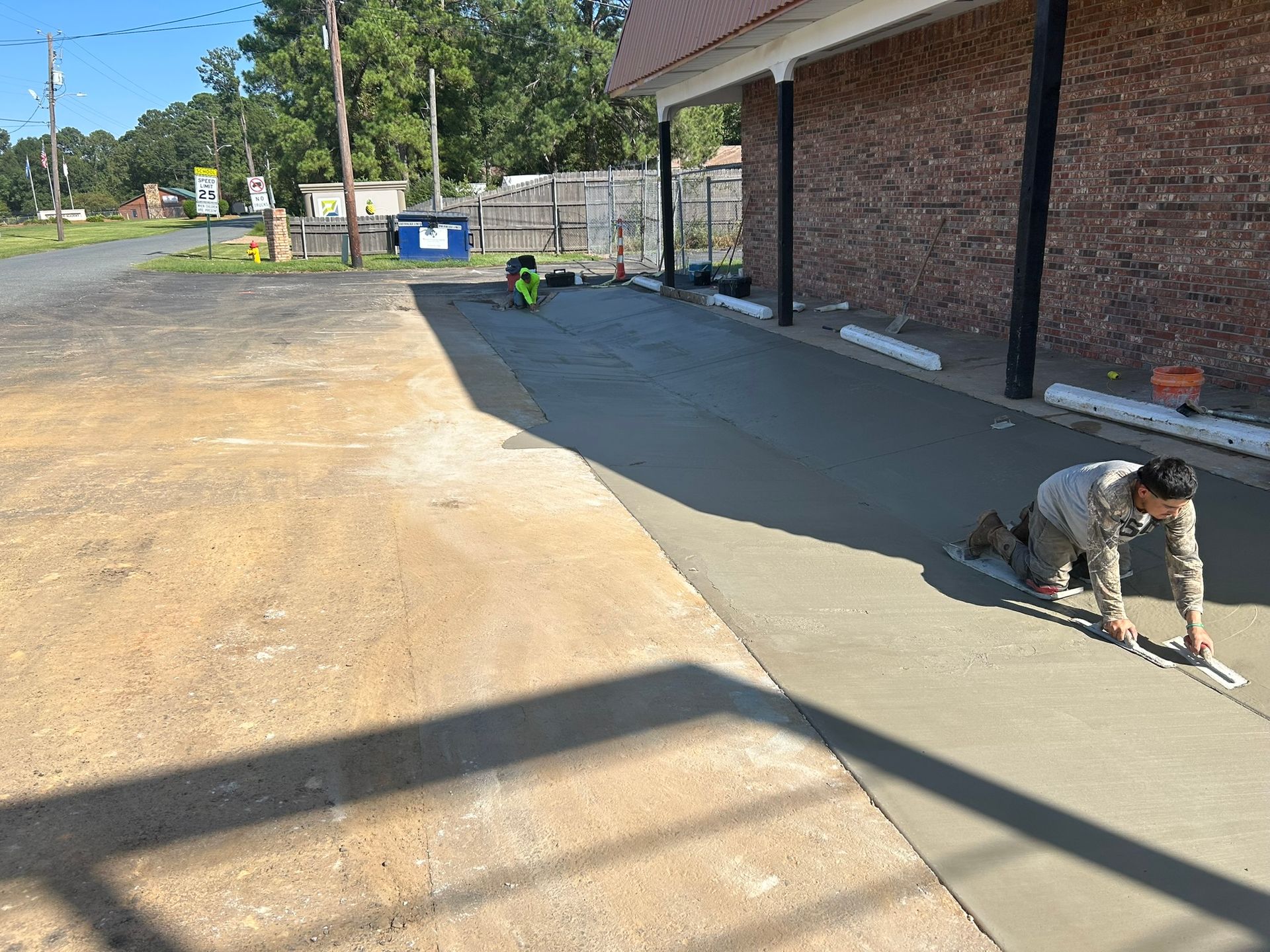 Workers smoothing wet concrete on a sidewalk next to a brick building.