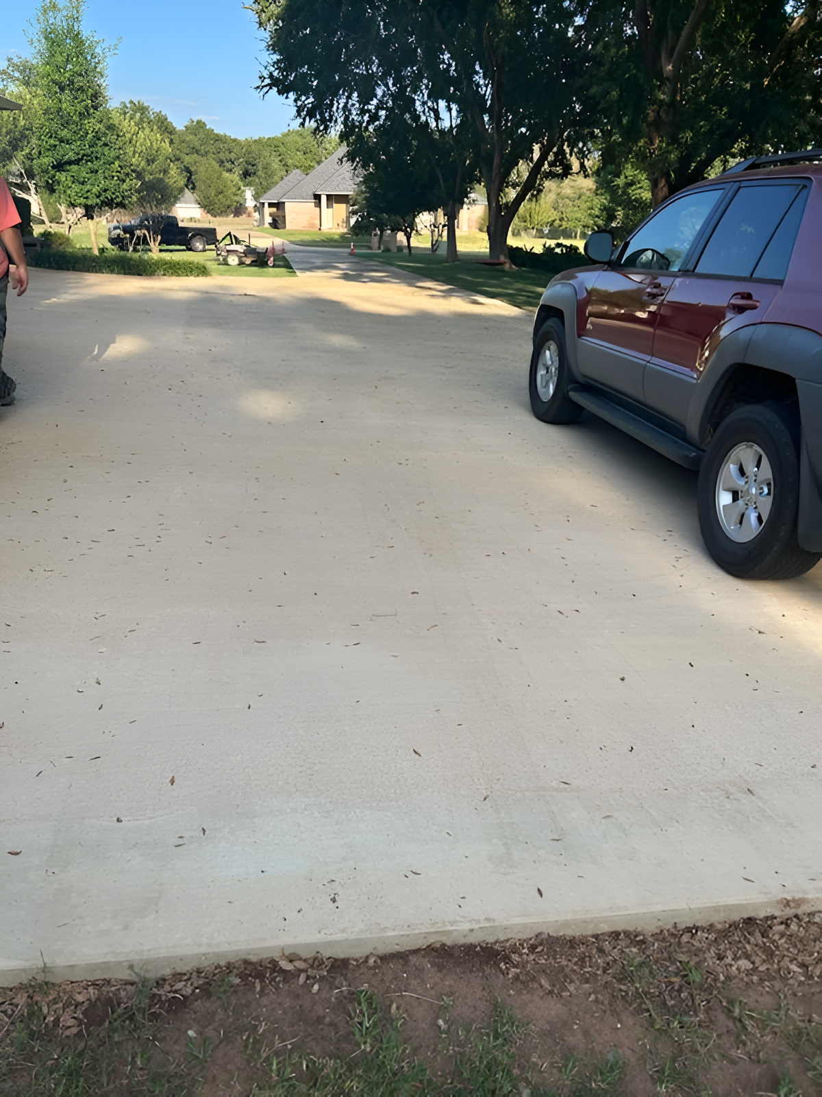 A red SUV parked on a light-colored concrete driveway with a person standing nearby; residential setting.