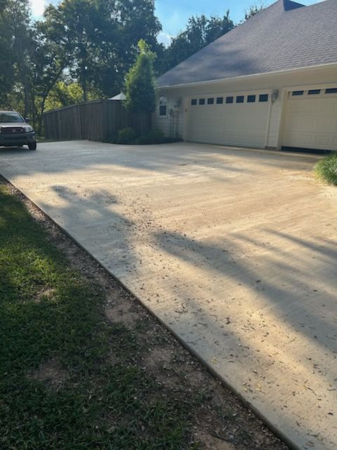 Concrete driveway leading to a house with garage doors. A vehicle is parked in the driveway.