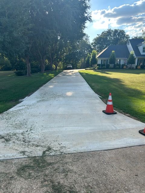 Newly poured concrete driveway with safety cones, trees, and house in the background.