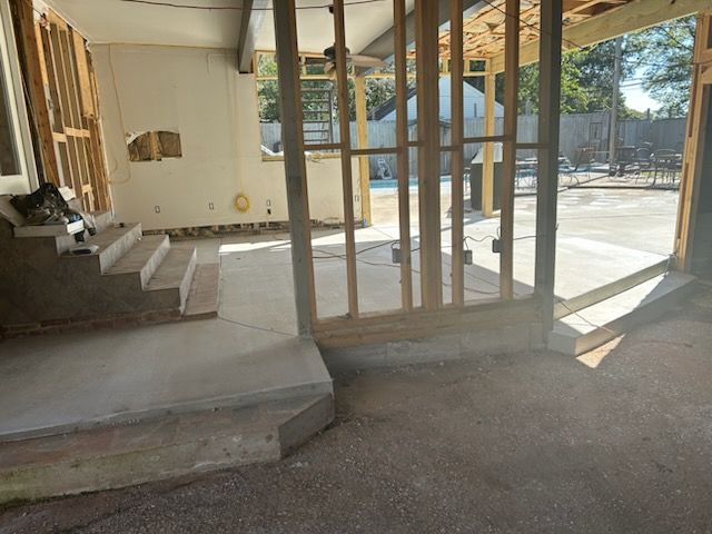 Interior renovation in progress. Concrete steps and floors, wooden framing, outdoor view.
