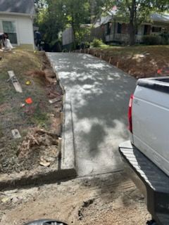 Freshly poured concrete driveway slopes upward towards a house; a truck bed is in the foreground.