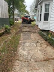 Concrete walkway with cracked surface, construction vehicle in background, beside a house.