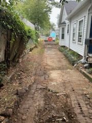 Dirt path between a wooden fence and a white house, showing tire tracks.