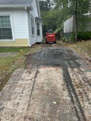 Driveway with concrete slabs and fresh asphalt. A small orange construction vehicle is in the background.