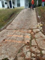 Cracked concrete driveway with orange spray lines, leading to a house. A person stands nearby.