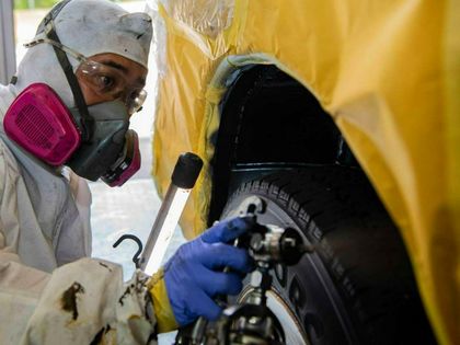 A man wearing a mask is spray painting a tire