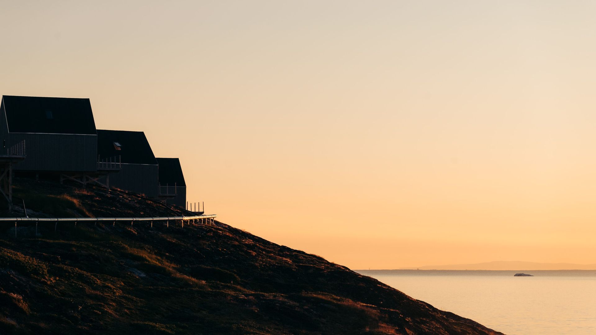 Huse på en bjergskråning har udsigt over havet ved solopgang med gylden himmel.