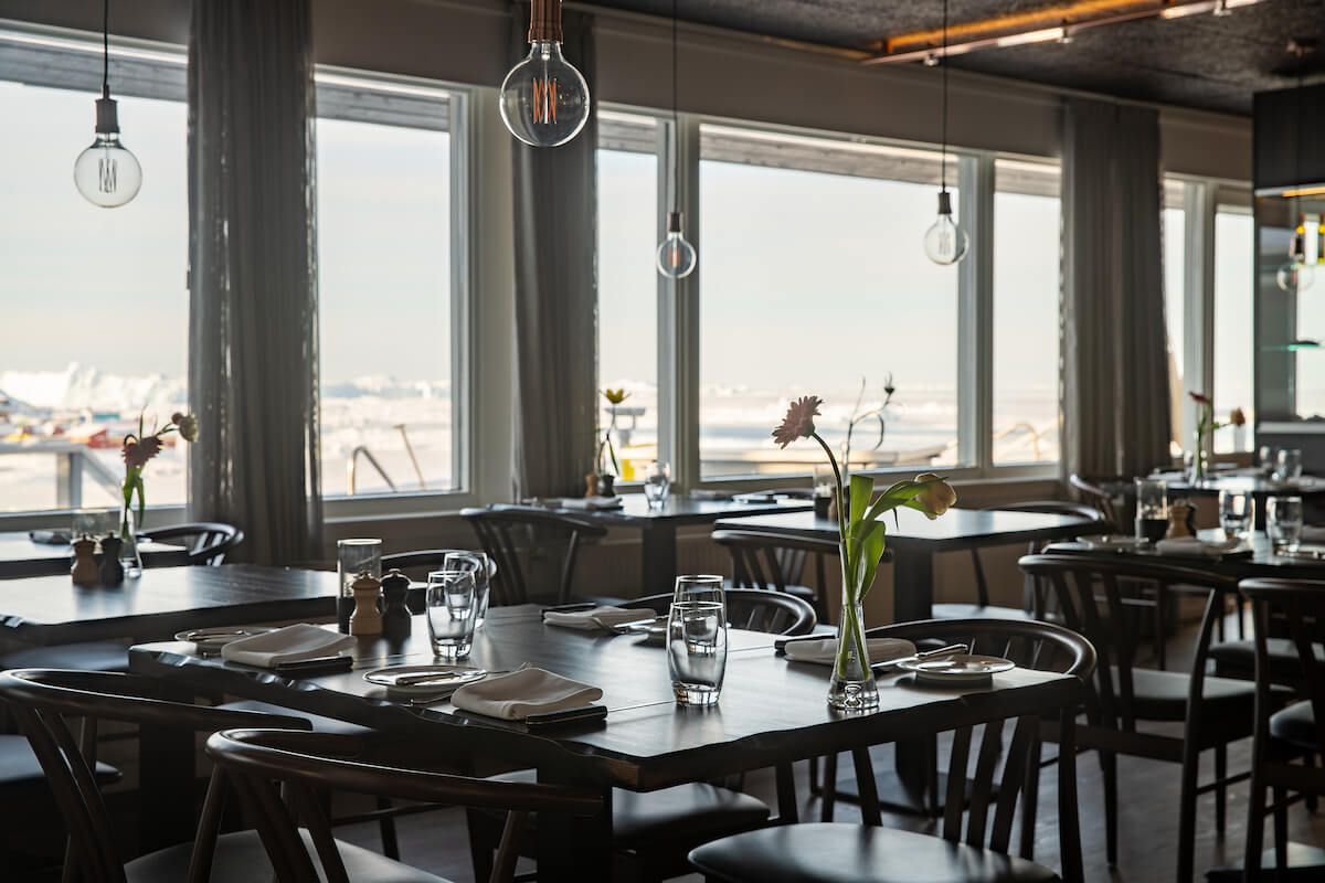Restaurantinteriør med dækkede borde, store vinduer og udsigt udover.