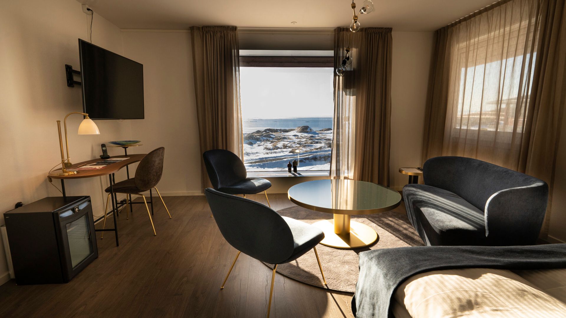Hotelværelse med skrivebord, stole, sofa, sofabord og stort vindue med udsigt.